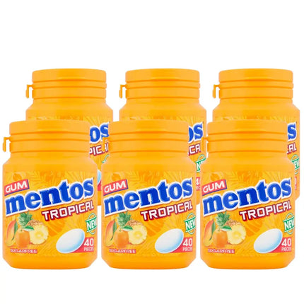 Six bottles of Mentos Gum Tropical chewing gum, each with a capacity of 56 grams and labeled as containing 40 pieces. The bottles are orange with the product name and images of tropical fruits displayed on the label.